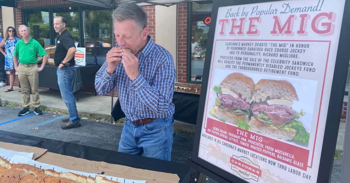 man eating a sandwich outdoors by a sign