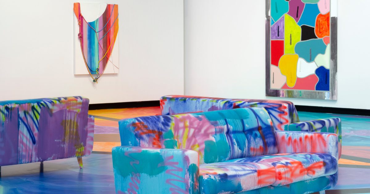 Colorfully tiedyed couches and floor with art pieces hanging on white walls