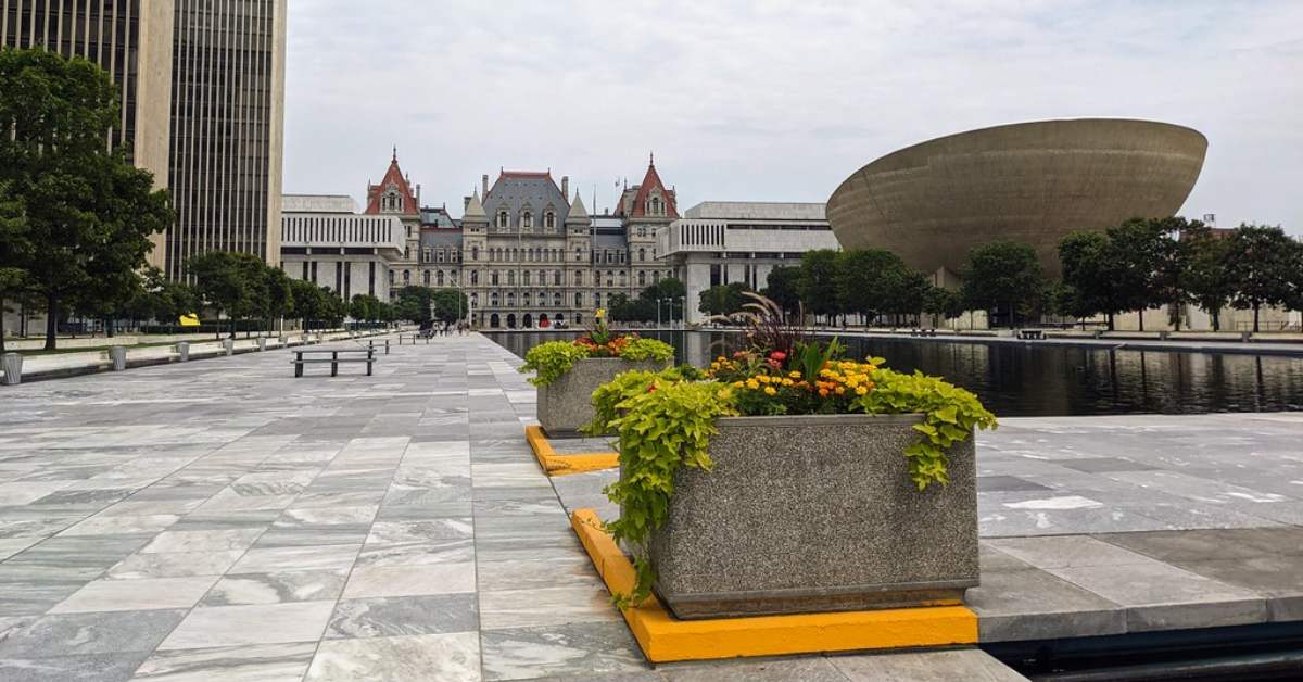 Large open plaza with large buildings in the background and colorful flower pot arrangements in the foreround