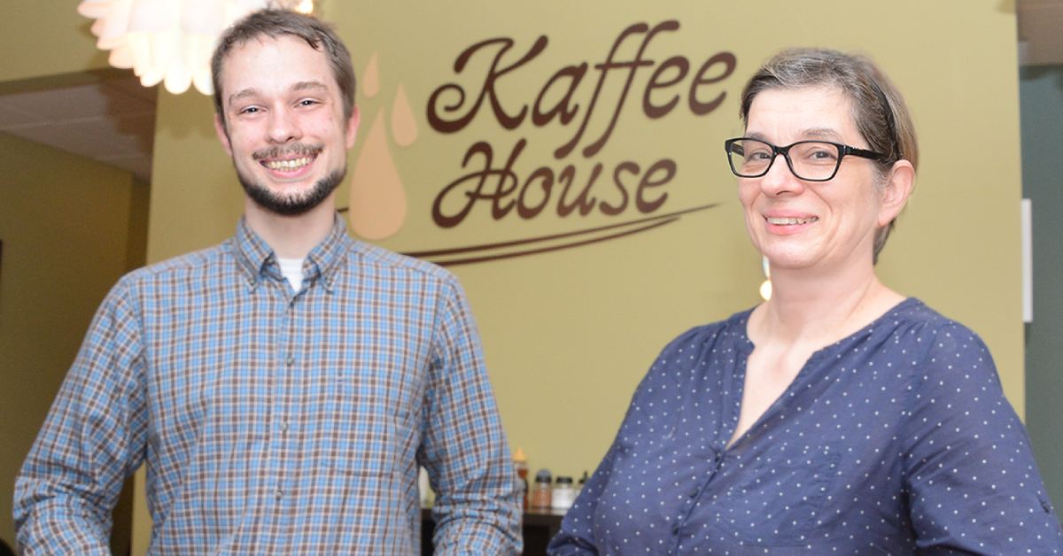 A man and woman standing in front of a wall with the KaffeeHouse logo