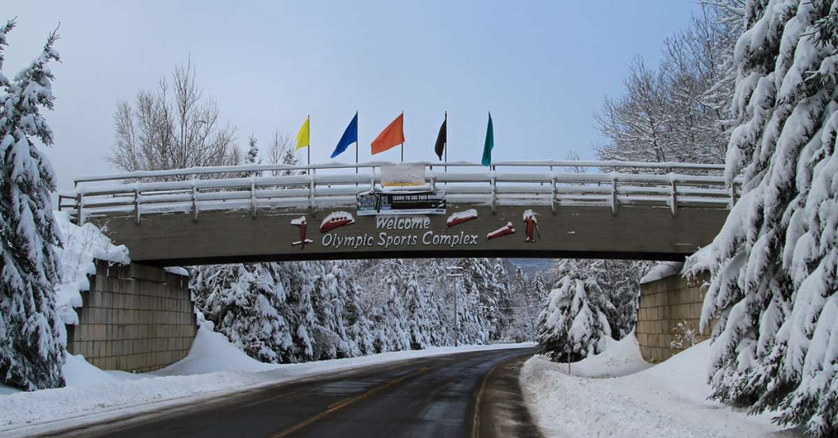 Bridge labeled welcome olympic sports complex with 5 flags of olympic colors