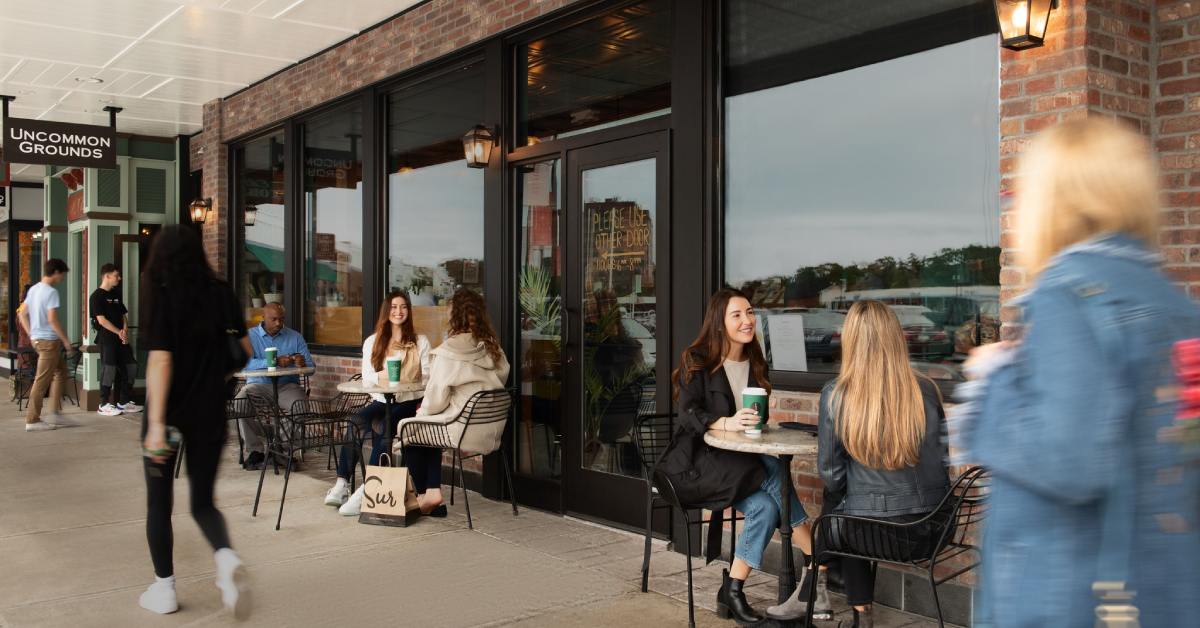 People walking in front of a store with people sitting at outdoor tables