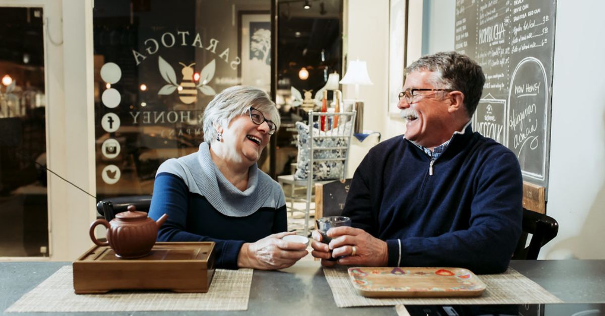 Couple sitting next to each other at a table laughing and holding drinks 