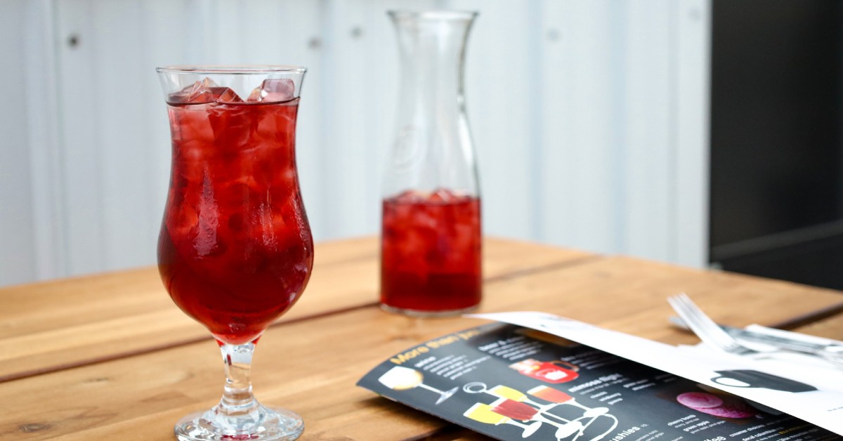 A glass of red iced tea next to a pitcher and menu on a table 