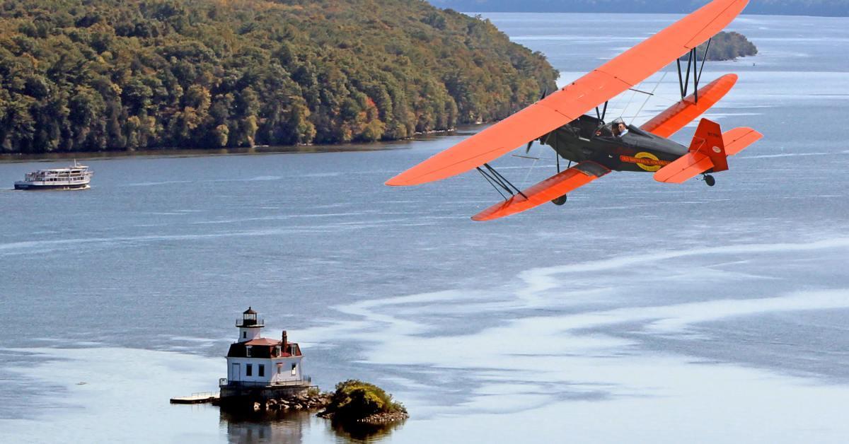 biplane flying over the water and a lighthouse