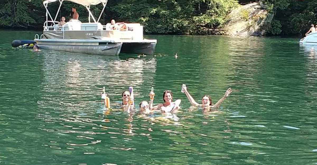 group of people swimming besides boat with drinks in hand