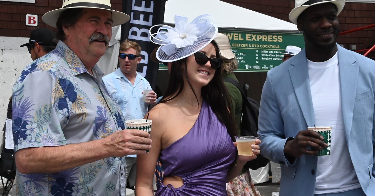 woman with fancy hat poses between two men at the track