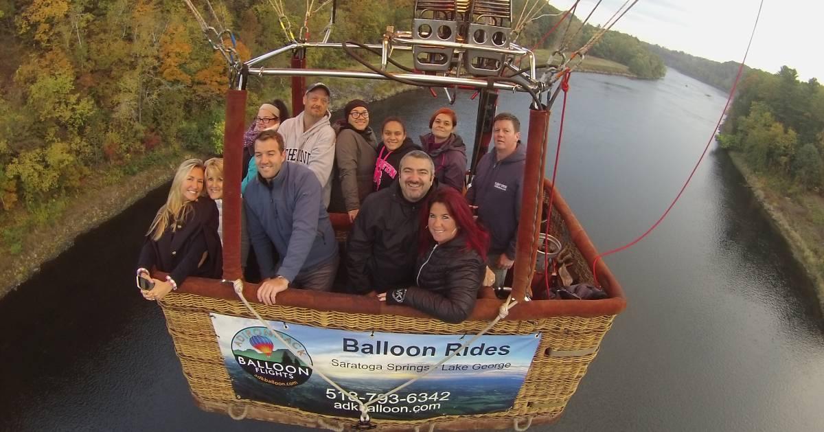 group of people smiling in hot air balloon going over water
