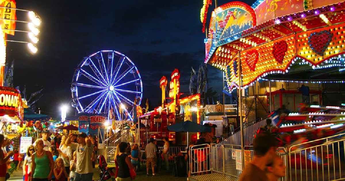 people walking a fair with lit up attractions at night