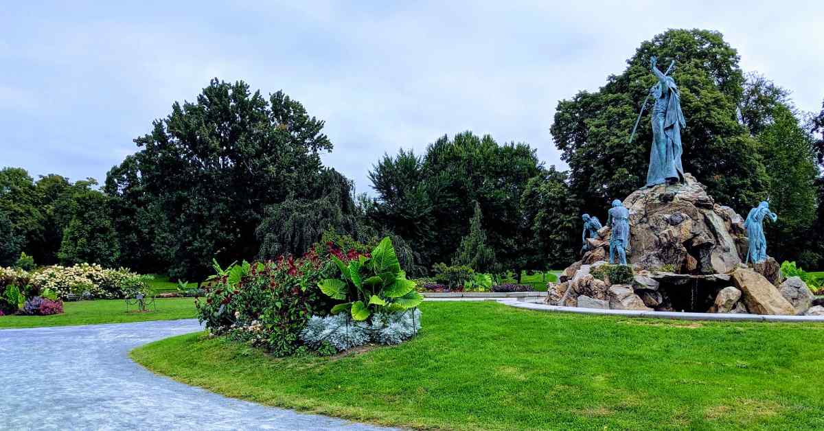 large plants and flowers in a public park with a large statue nearby