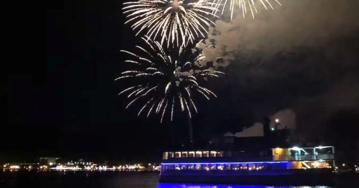 fireworks in the sky with a boat passing underneath them on water