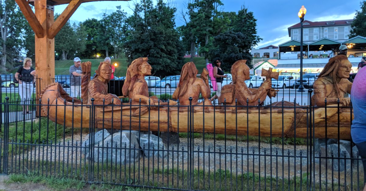 wooden canoe carving with trappers and indians in front of fort william henry