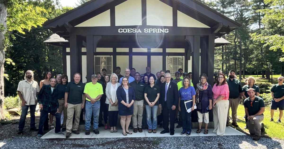 large group of people smiling for photo in front of newly rebuilt coesa spring house