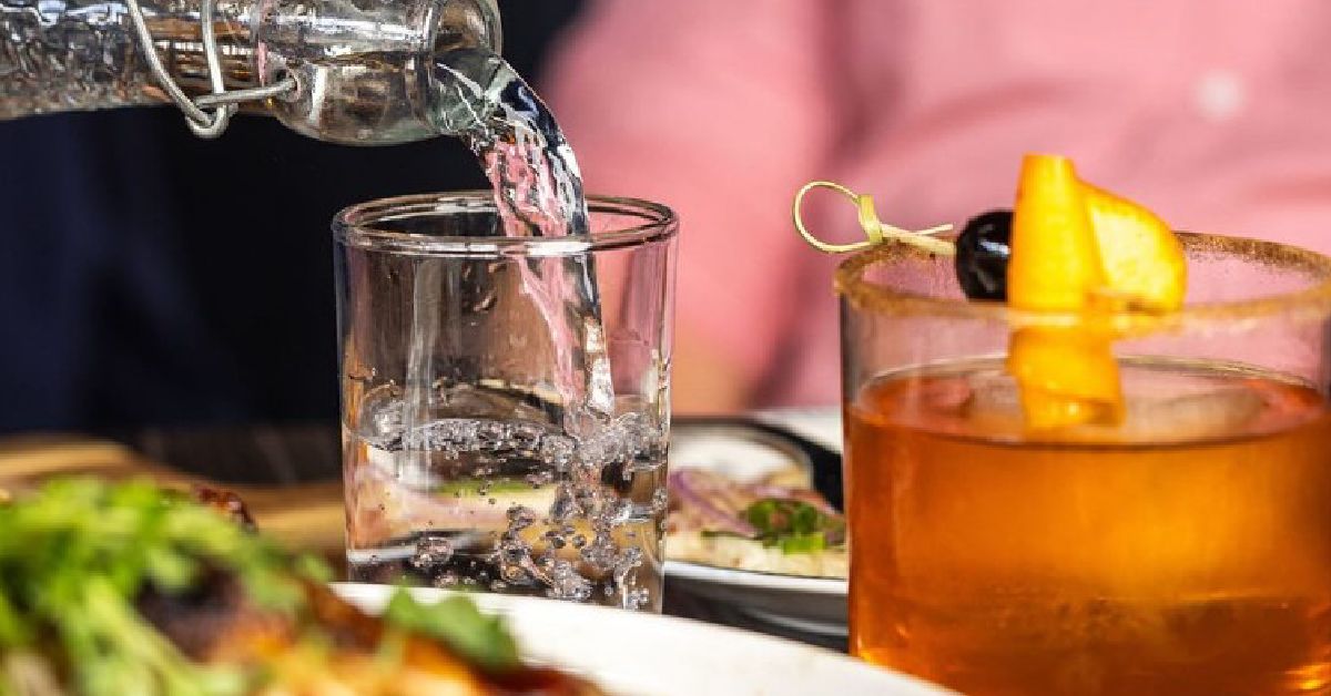 water being poured into cup besides a craft cocktail