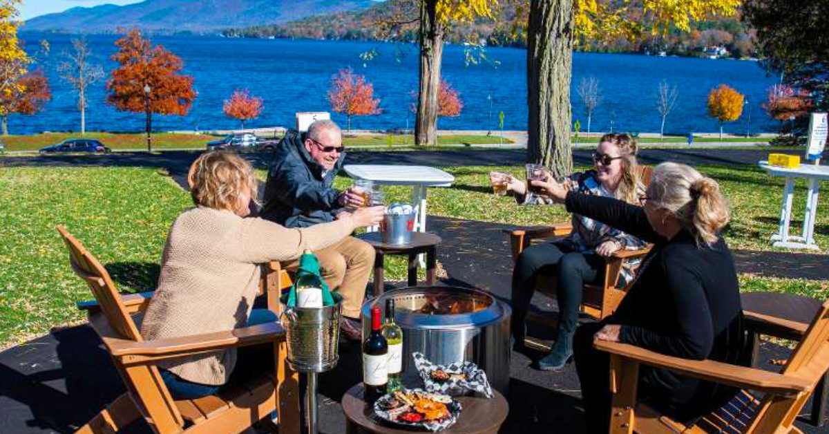 four people 'cheersing' around outdoor fire pit set against fall backdrop