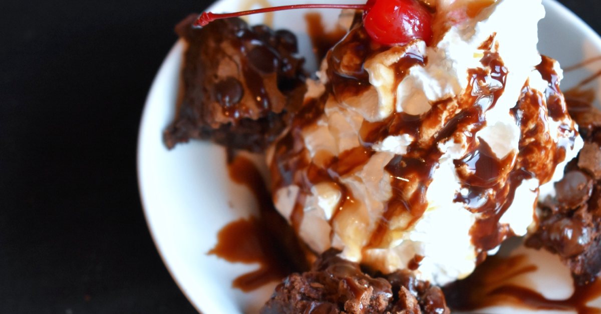 brownie sundae with whipped cream, chocolate drizzle, and a cherry