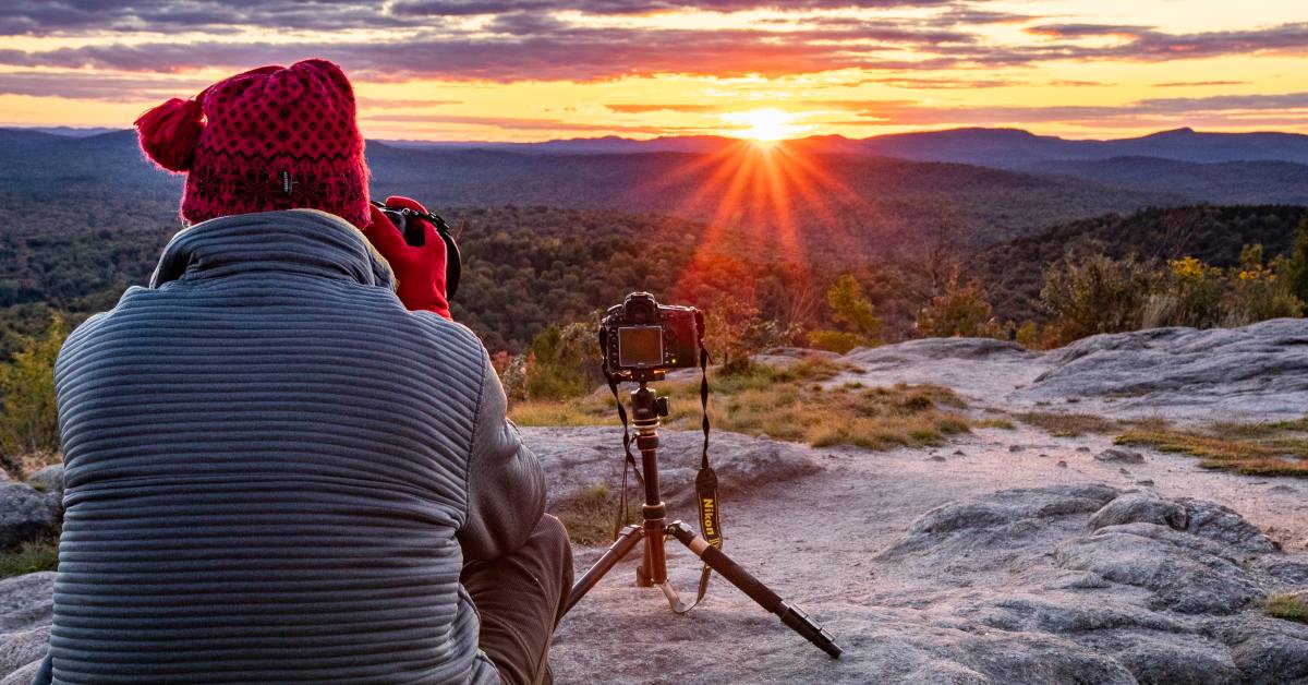 woman takes photo from mountain summit during susnet