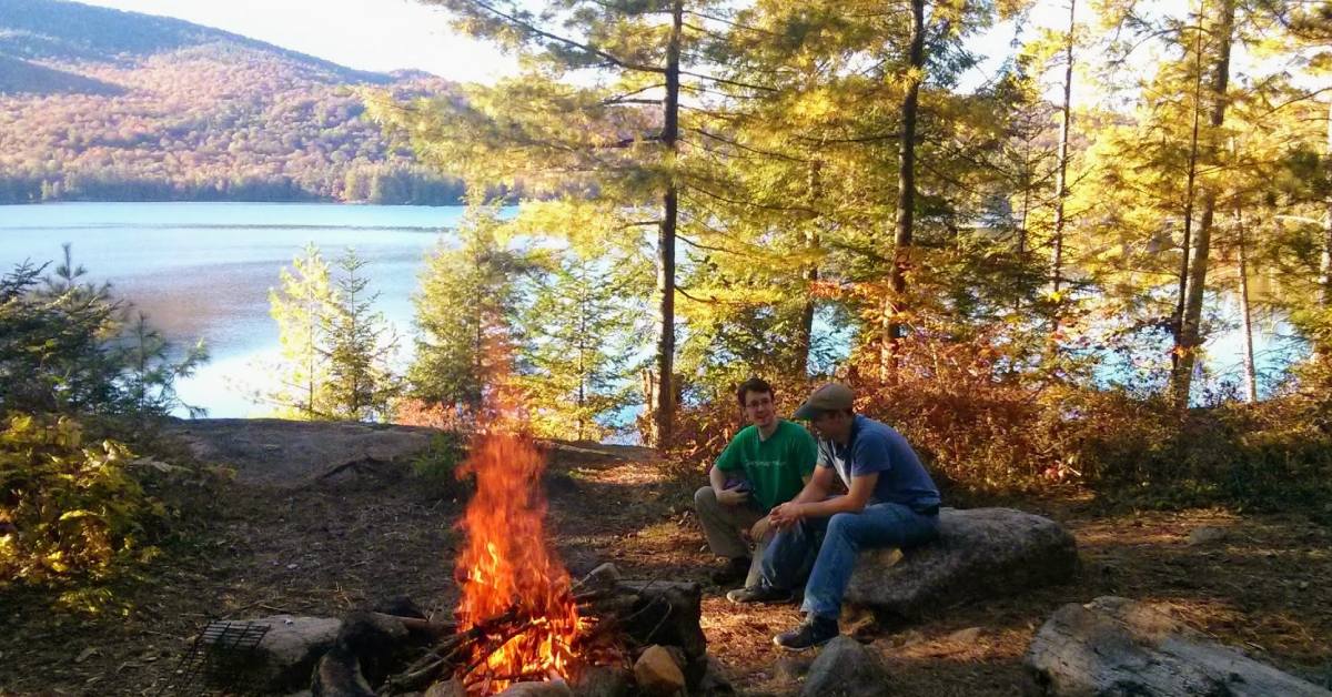 two men camping in fall by fire