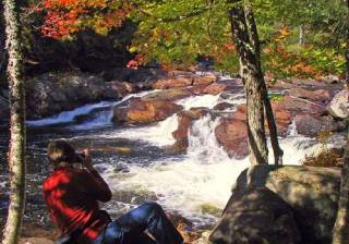 man photographs small waterfall in fall