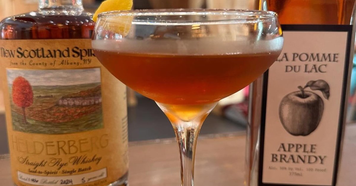 bottle of whiskey and apple brandy next to a cocktail glass