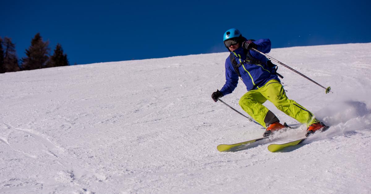 a downhill skier in a blue coat and lime green pants