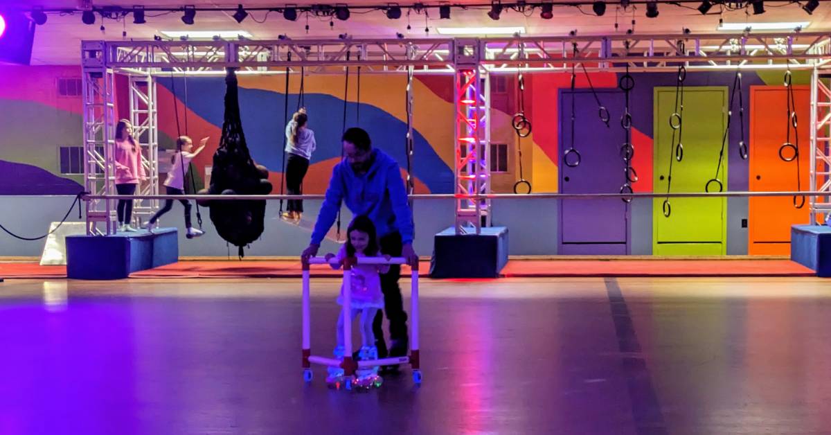 dad and little girl skating together, ninja course in background at the fun spot