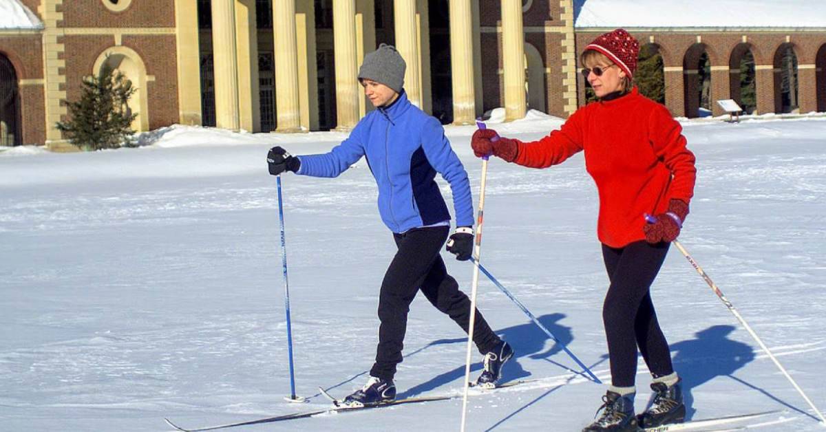 two people cross country skiing on snowy ground by a historic building