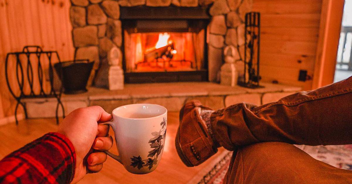 hand holding coffee cup in front of roaring fire