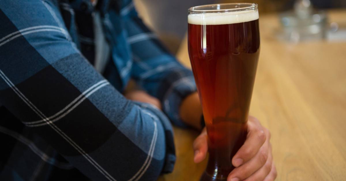 person in plaid shirt holding a beer glass