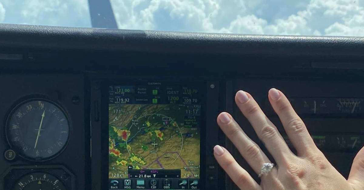 hand with engagement ring held up in front of controls on a plane