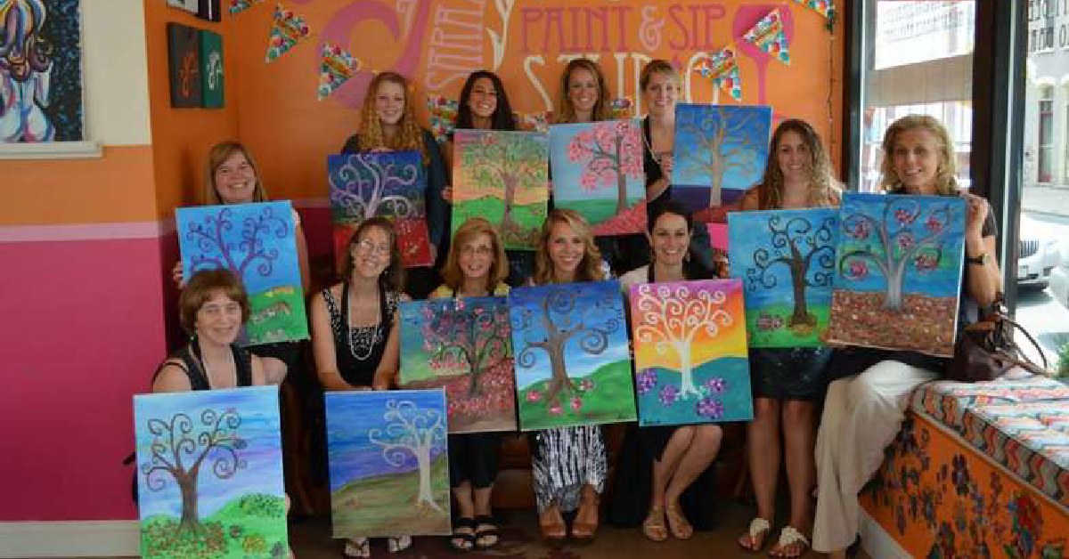 group of women holding tree paintings after class