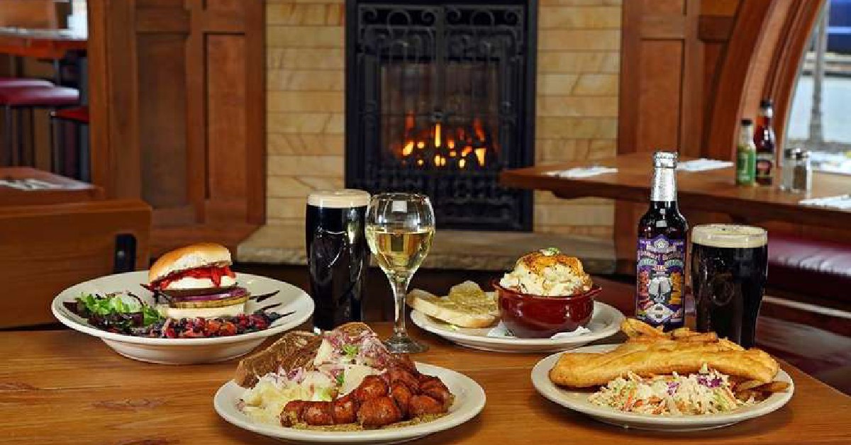food, beers, and wine on a restaurant table with a fireplace in the background