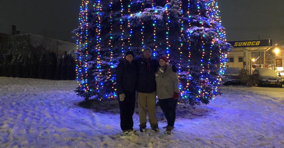 three people standing by a large Christmas tree with lights