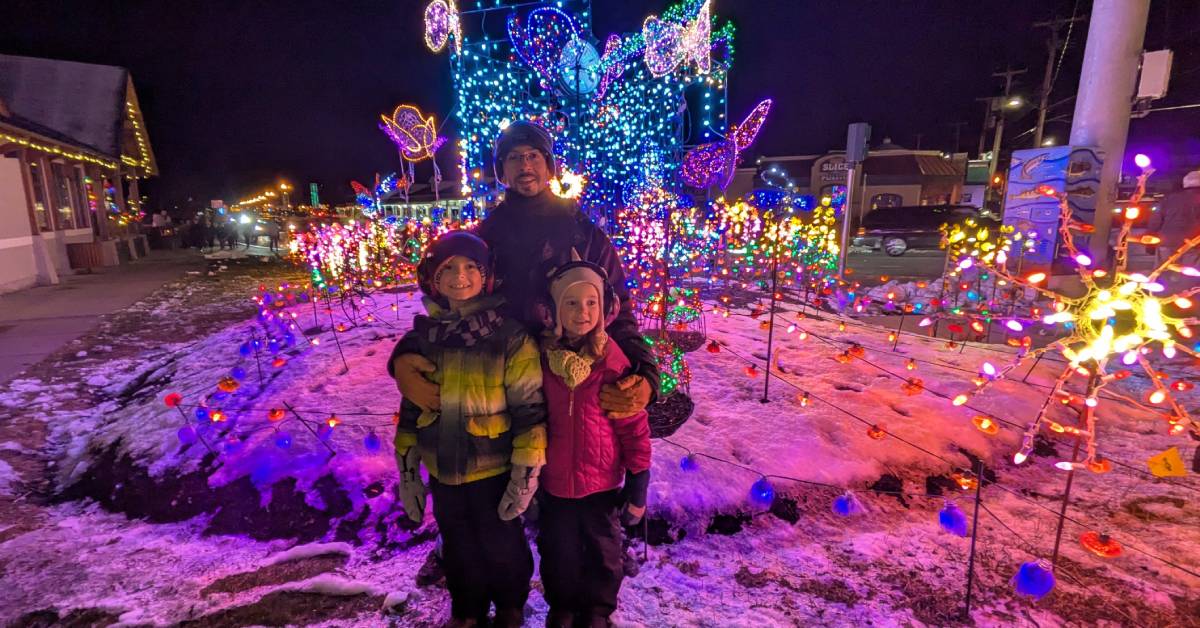 dad poses with kids in front of holiday lights in lake george