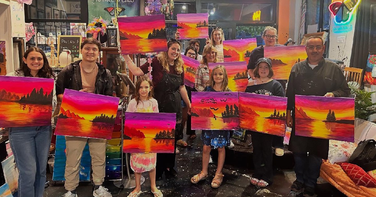 adults and children holding up sunset paintings