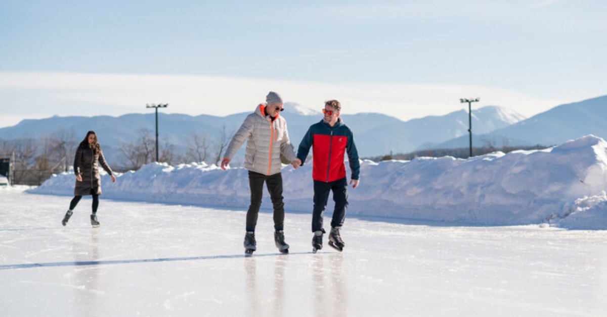 two men ice skating on an outdoor rink with a woman in the background