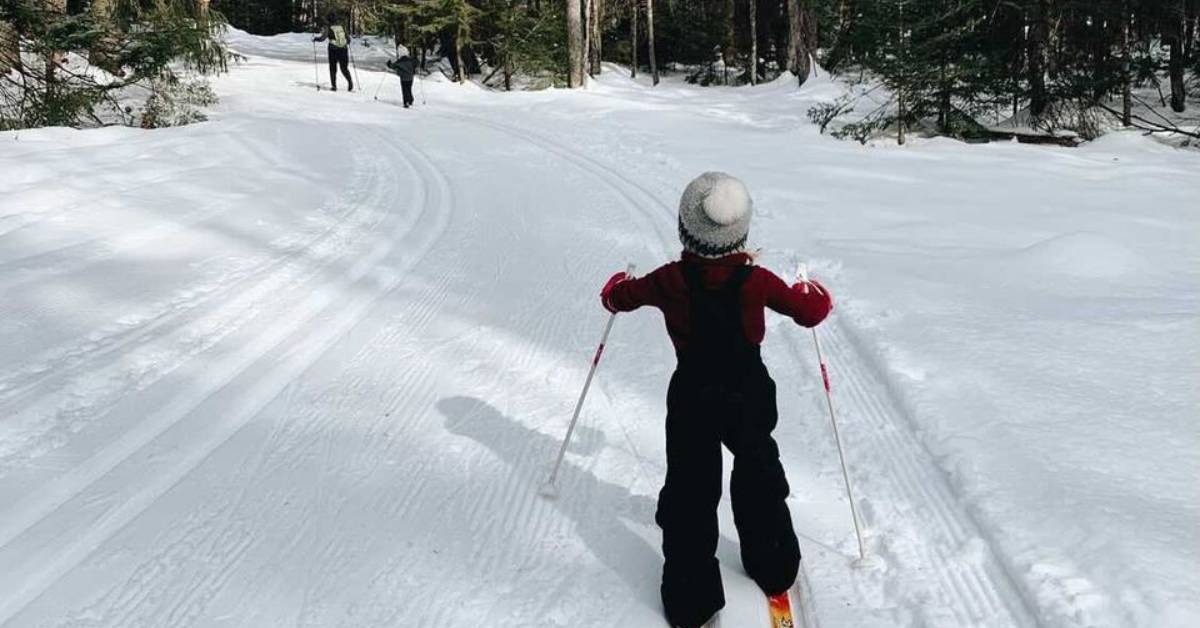 kid cross-country skiing behind parents