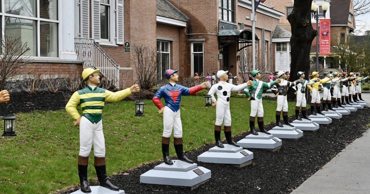 Colorful miniature jockey sculptures stand in a row outside the National Museum of Racing in Saratoga Springs, each painted in vibrant uniforms representing famous racing stables.