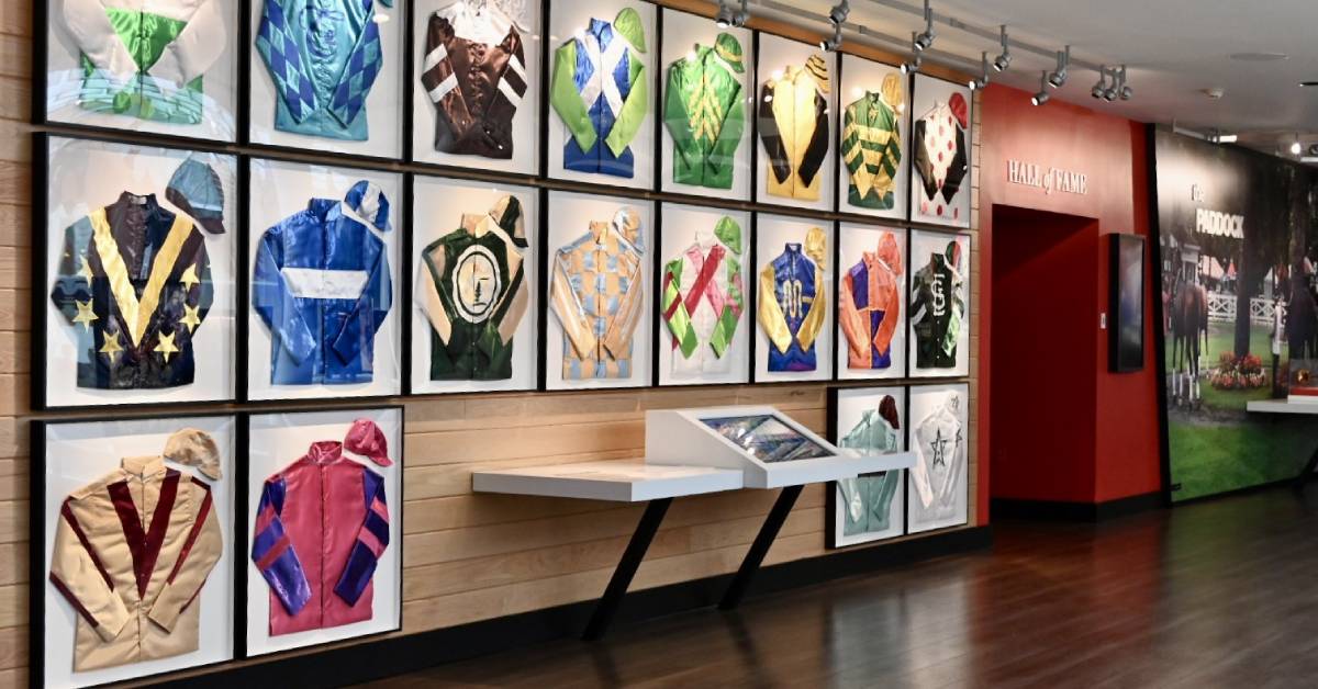 A wall full of colorful jockey jackets, each with its own unique design, representing legendary riders and racing stables.