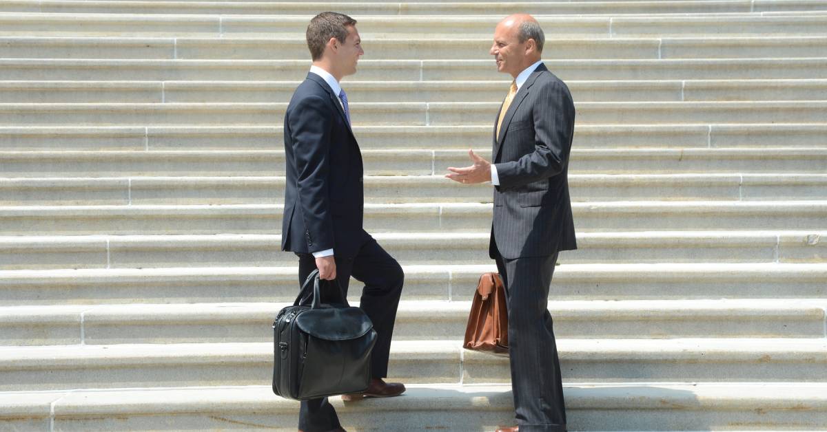 two men in suits and ties talk on stairs