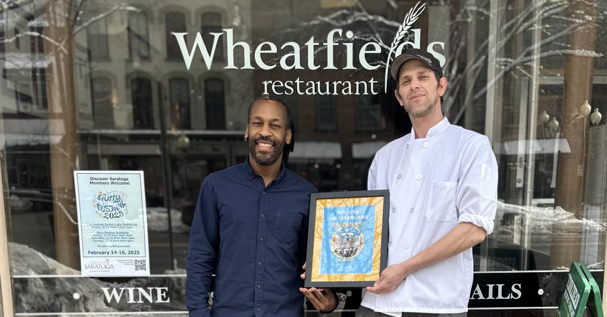 two men stand in front of wheatfields restaurant with award