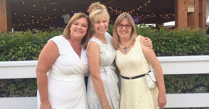 three women posing in front of what looks like a barn, all dressed in white