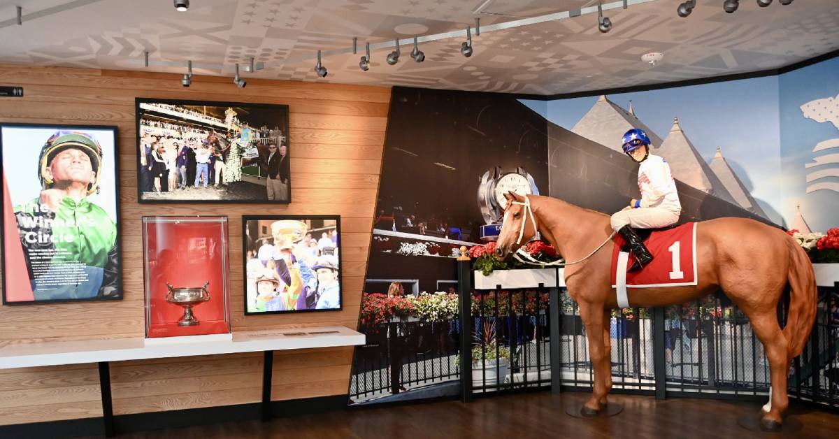 A life-sized racehorse exhibit with a jockey, racing photos, and a trophy at the National Museum of Racing.