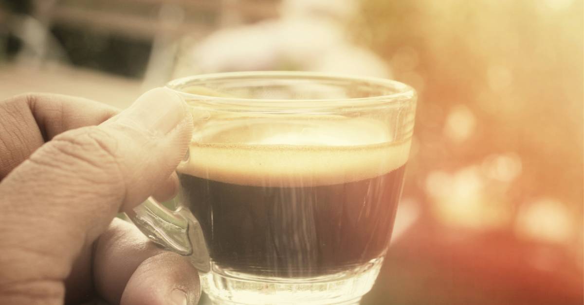 hand holding coffee in glass cup outdoors