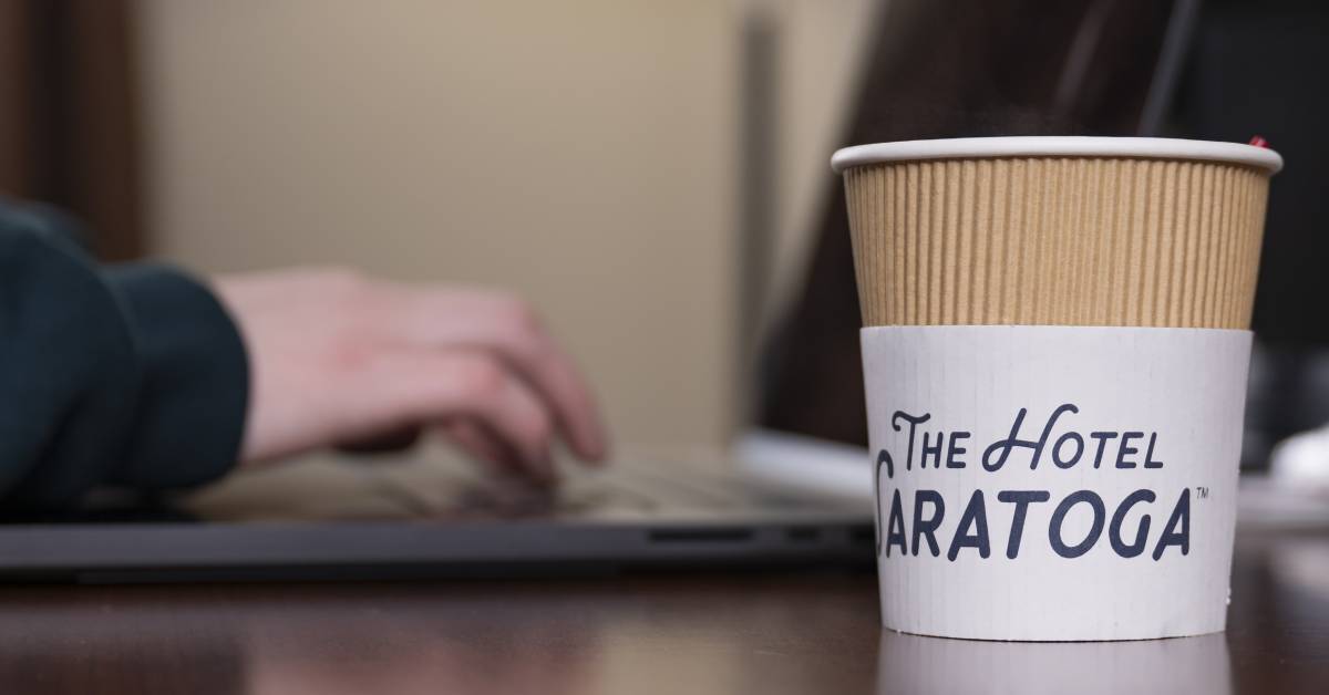 hotel saratoga coffee cup by someone using a laptop