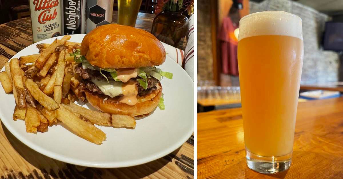 A hearty burger with melted cheese, lettuce, and sauce sits on a plate with crispy fries, accompanied by a tall, hazy beer at Henry Street Taproom