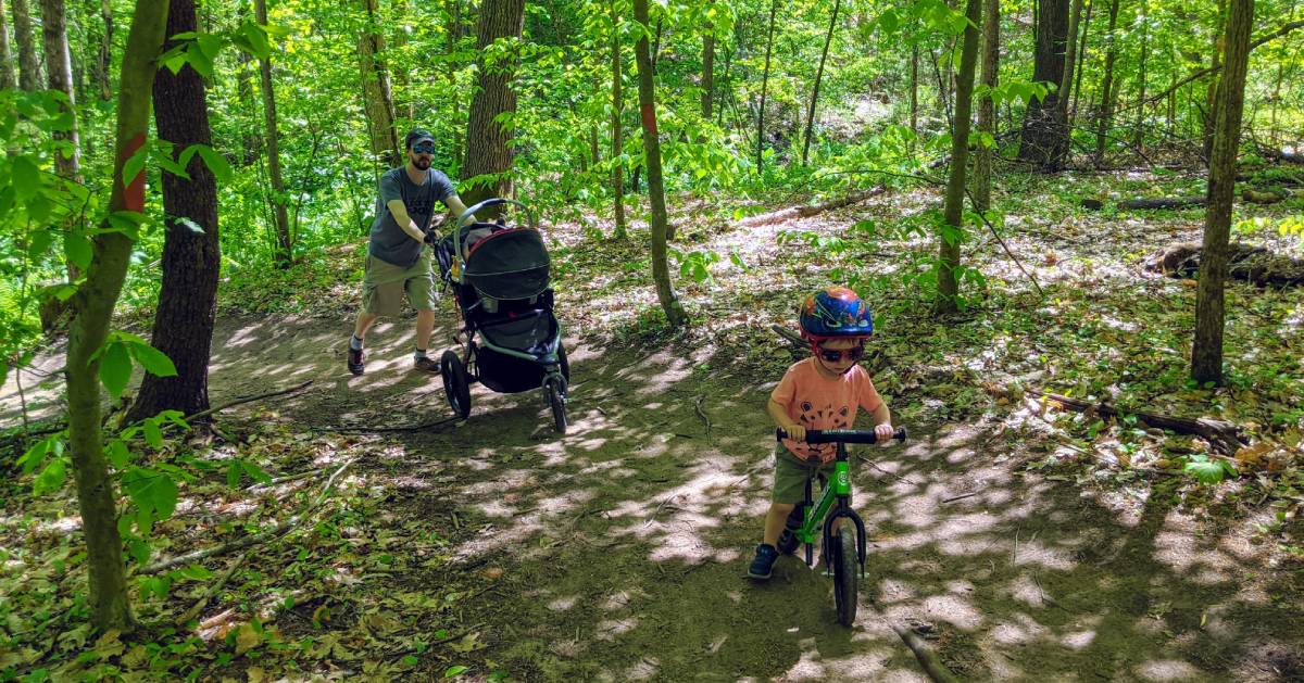 little boy on bike, dad behind pushing stroller