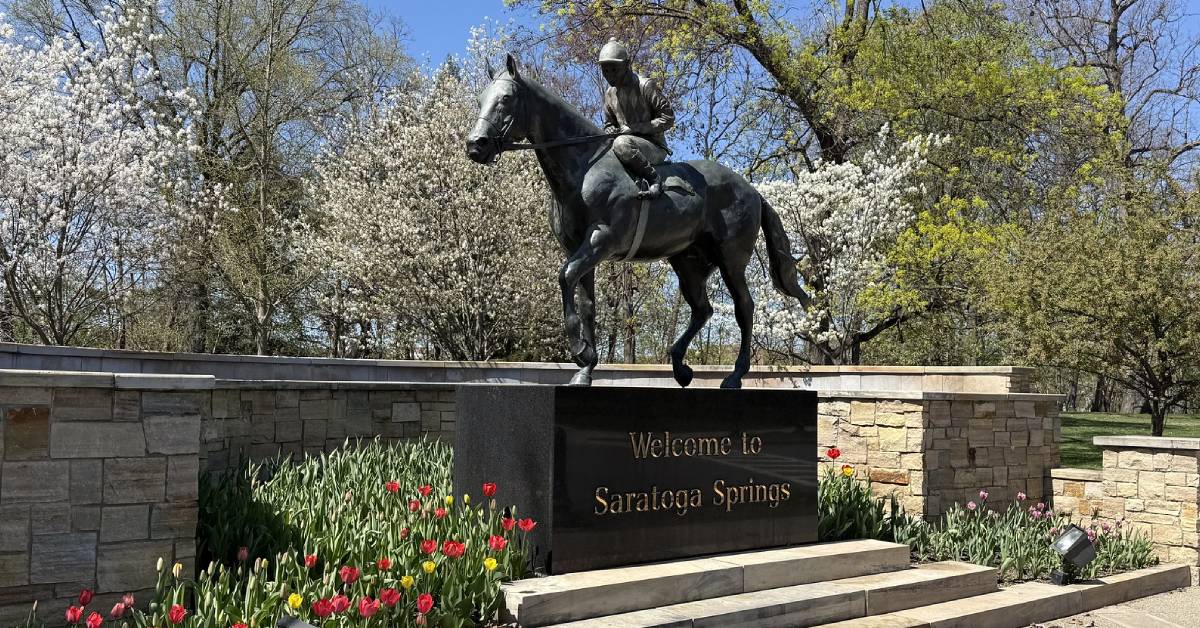welcome to saratoga springs sign with horse and jockey statue
