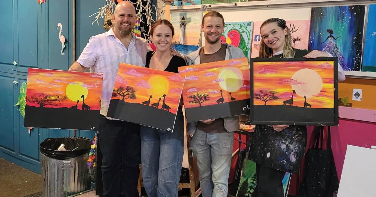 four people holding up sunset paintings