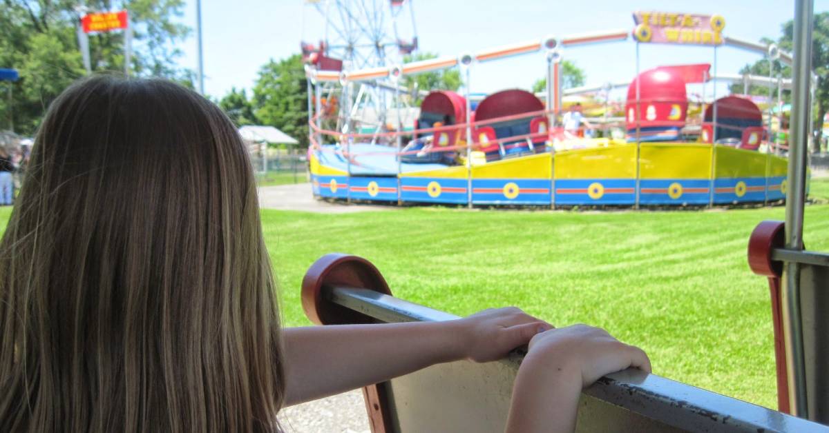 back of little girl on train ride looking at tilt-a-whirl ride at hoffman's playland in latham
